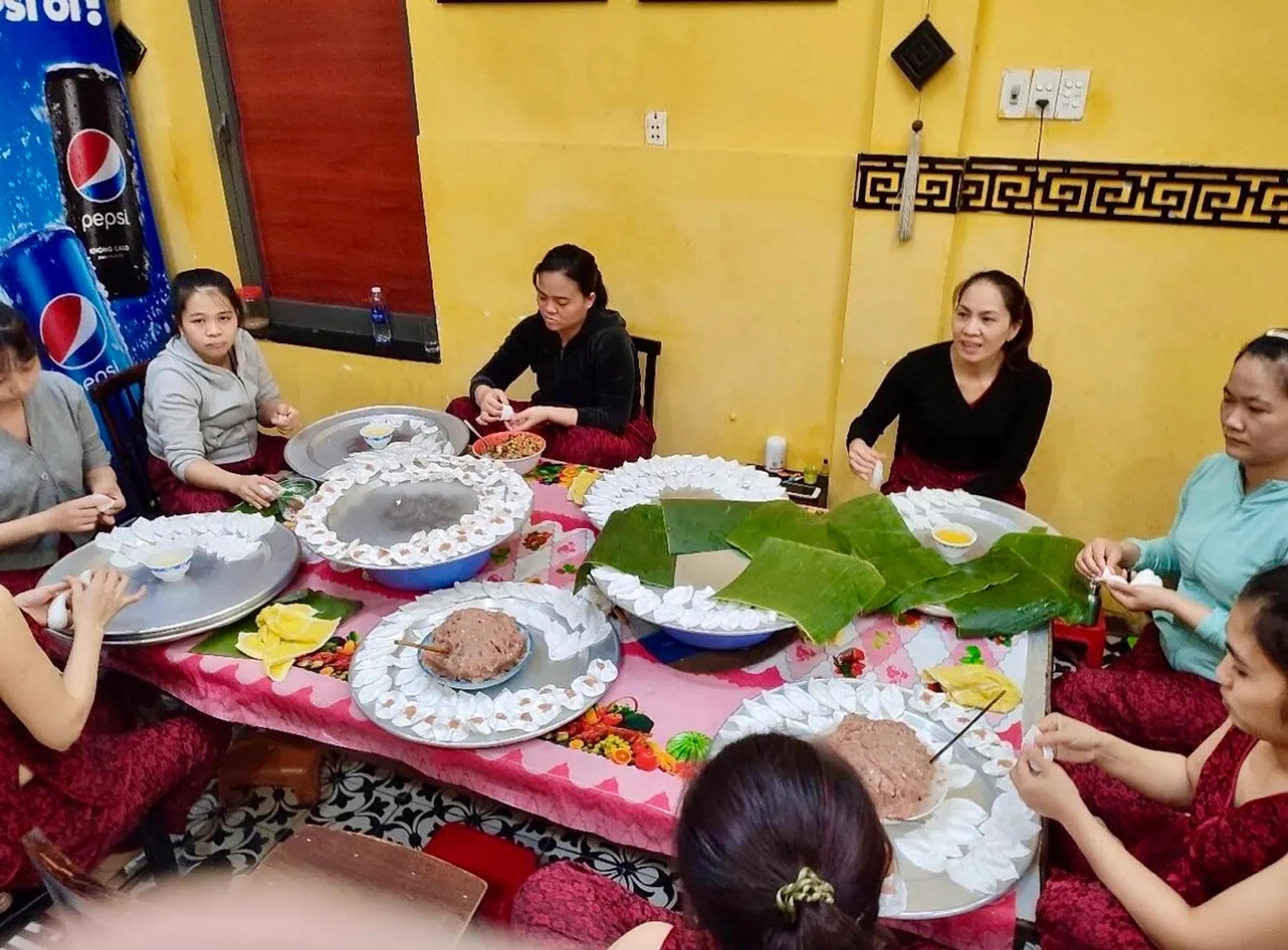 Local cooks folding white rose dumplings around a shared table in a Hoi An family kitchen