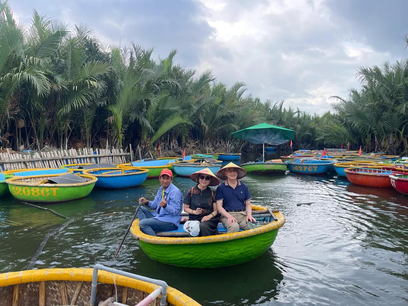 Two guests in conical hats being rowed in a green basket boat through the coconut palm forest near Hoi An