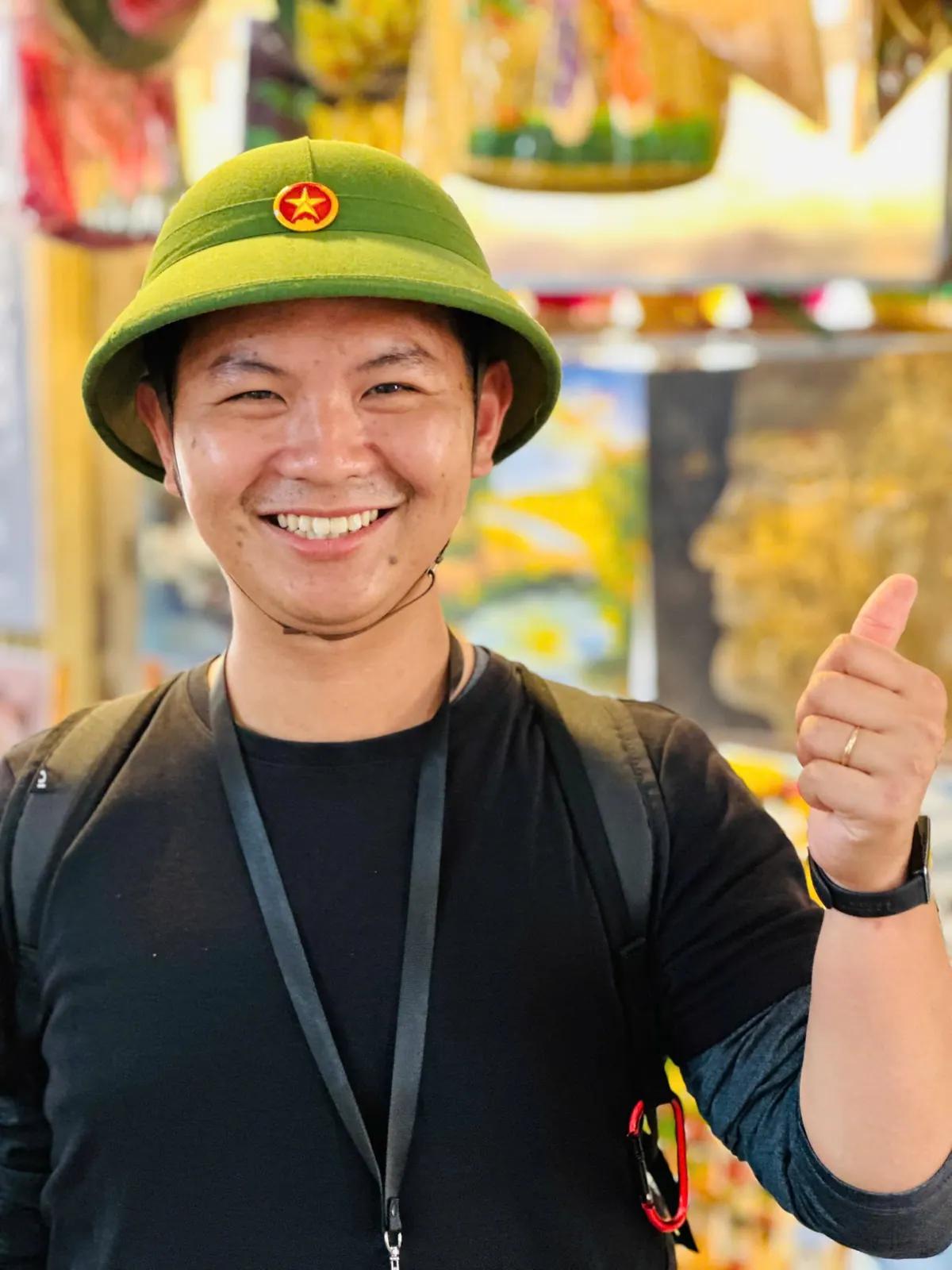 Toàn (Tom), licensed local guide in Hoi An, smiling with a thumbs up in a green Vietnamese pith helmet