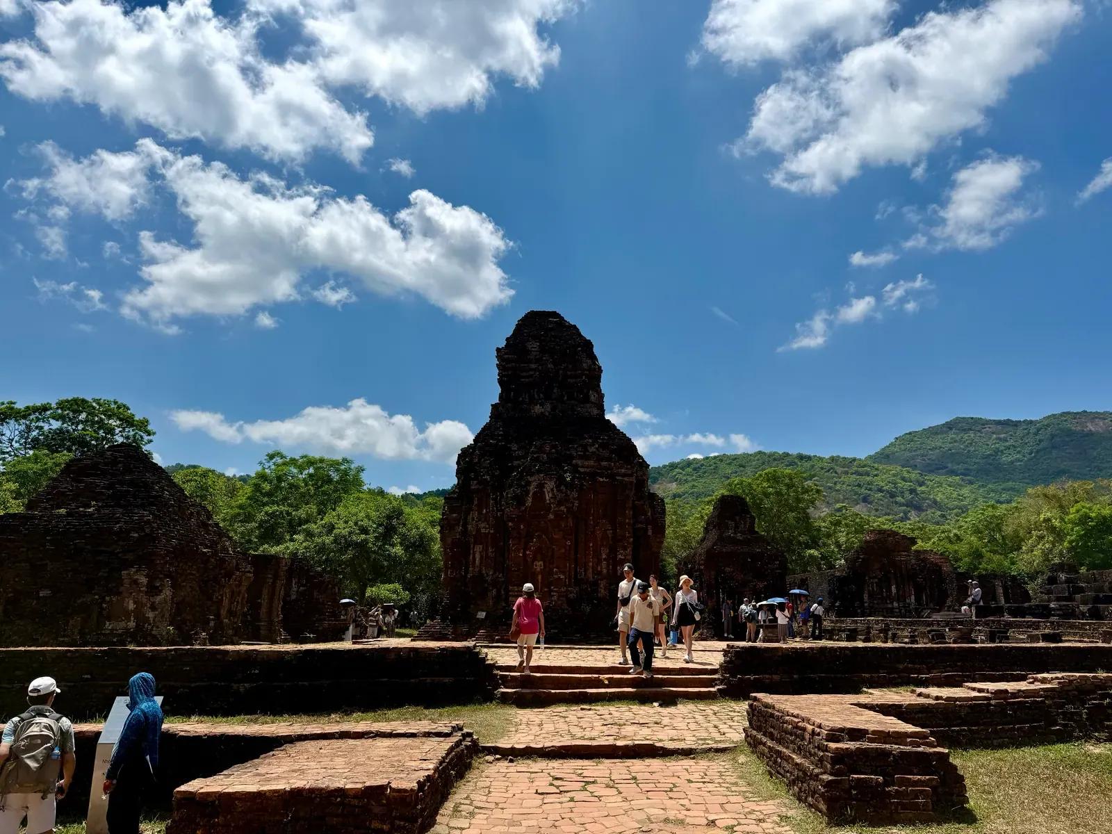 Visitors walking among the red-brick Cham towers of My Son Sanctuary under a bright blue sky