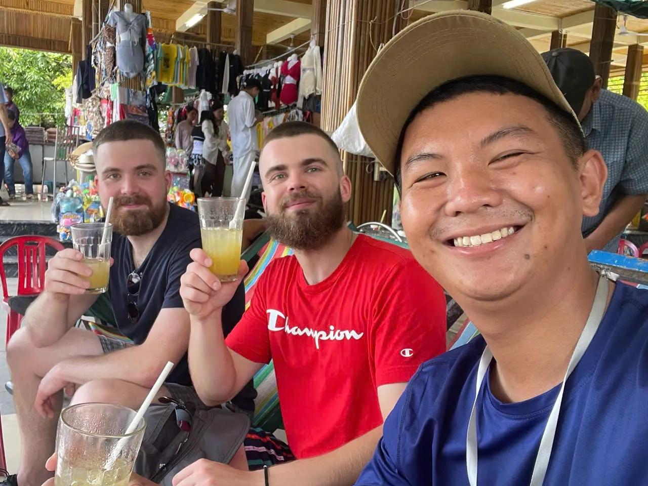 A local guide and two guests raising glasses of fresh juice at a Hoi An market stall