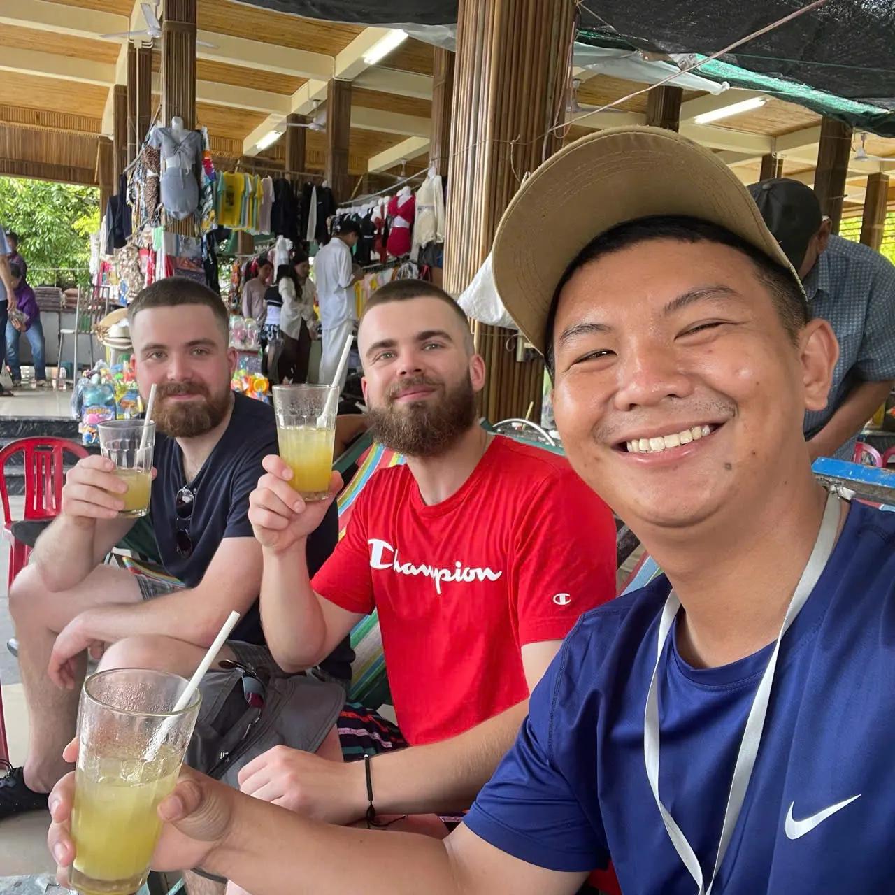 A local guide and two guests raising glasses of fresh juice at a Hoi An market stall