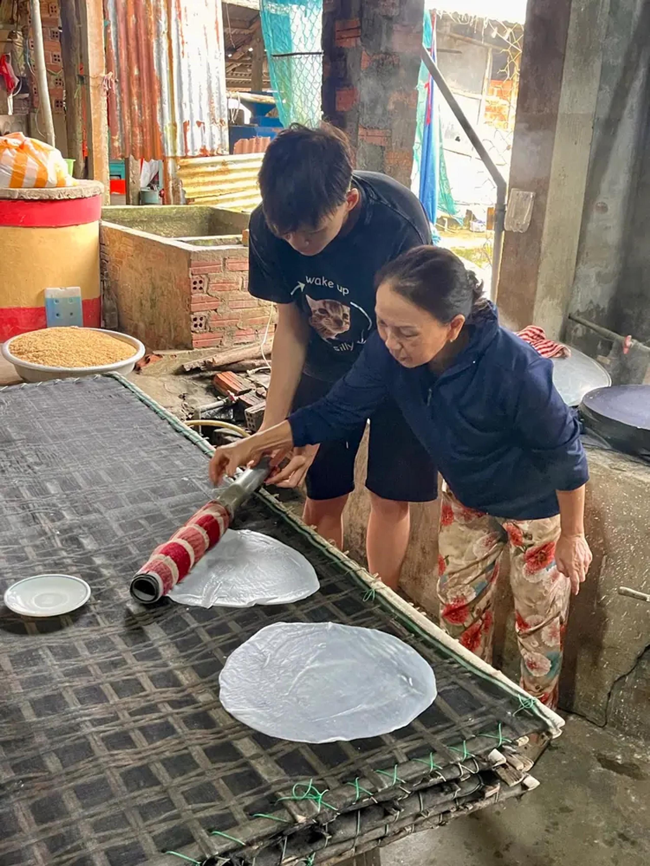 A guest rolling a steamed rice sheet with the host at a family noodle workshop near My Son