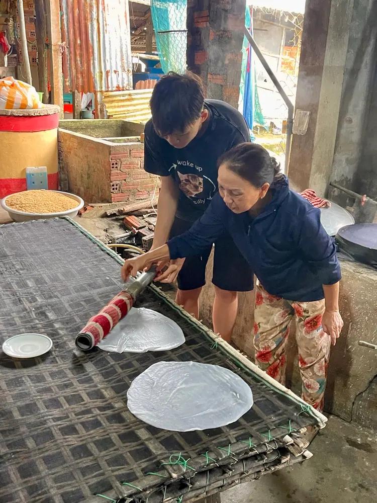 A guest rolling a steamed rice sheet with the host at a family noodle workshop near My Son