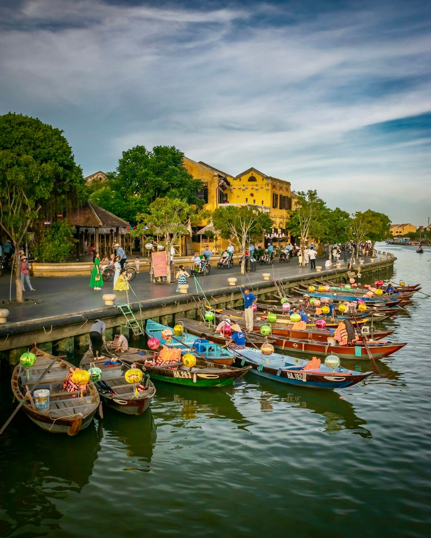Wooden boats hung with lanterns moored along the Thu Bon River in Hoi An Ancient Town, yellow houses behind