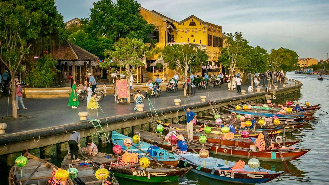 Wooden boats hung with lanterns moored along the Thu Bon River in Hoi An Ancient Town, yellow houses behind