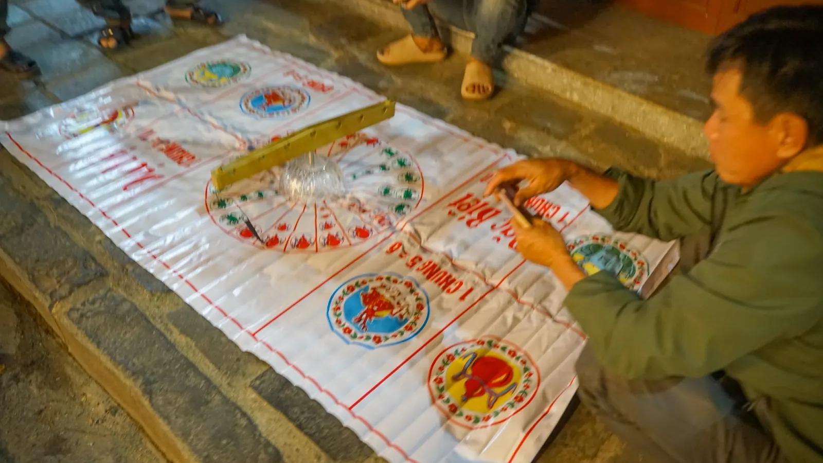 A Bau Cua mat spread on the pavement at night, the glass bowl in the middle and players crouched around it
