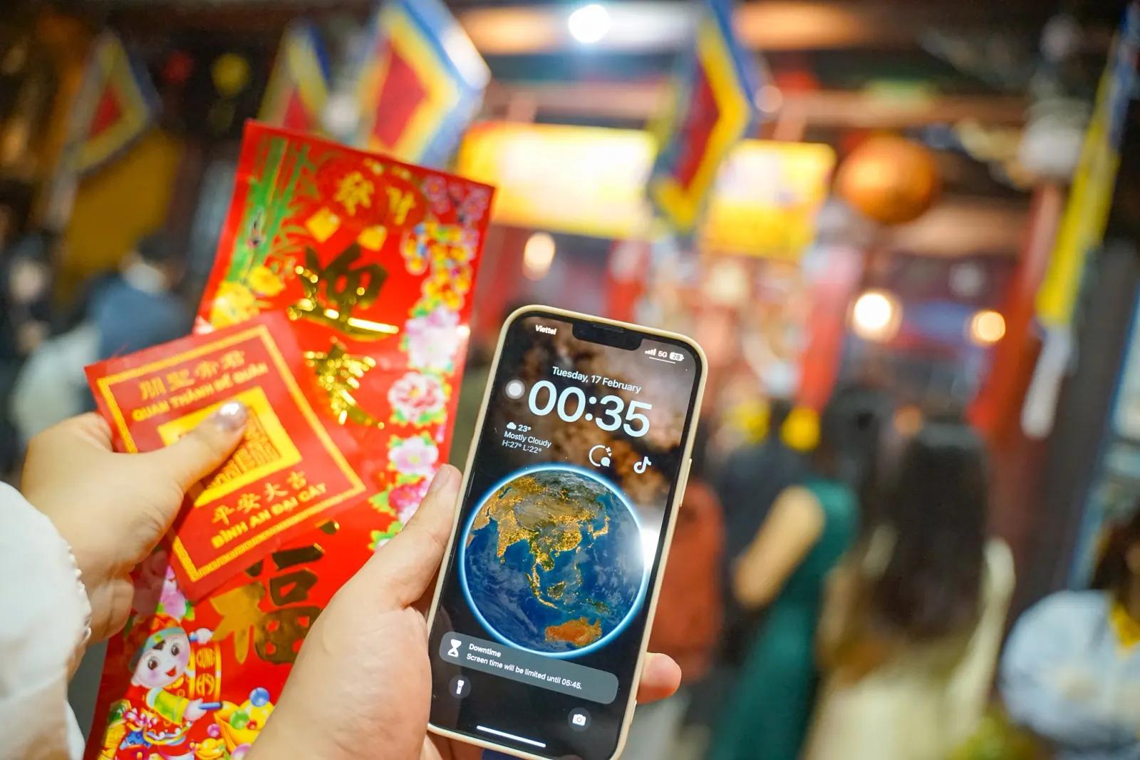 Hand holding a red fortune envelope in the temple, phone screen reading 00:35 on the first morning of Tet