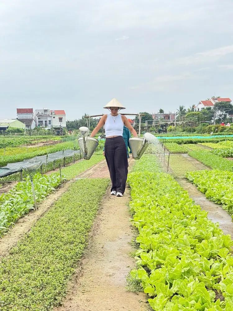 Carrying watering cans on a yoke between the herb beds at Tra Que vegetable village
