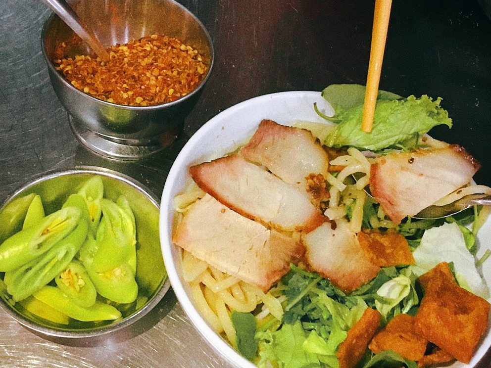 A bowl of cao lầu with sliced pork, greens and crispy crackers, fresh chili on the side, at Quán Cao Lầu Thanh