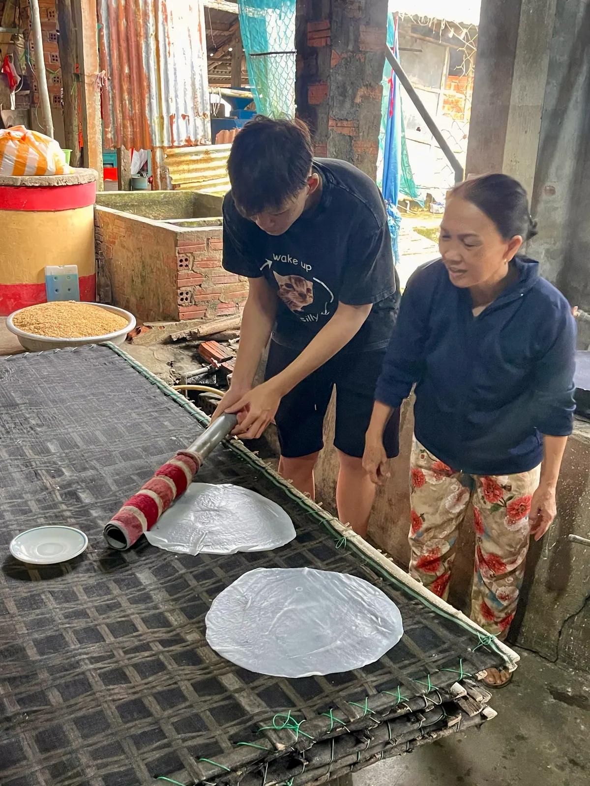A guest lifting a steamed rice sheet off the cloth with the family who makes the noodles