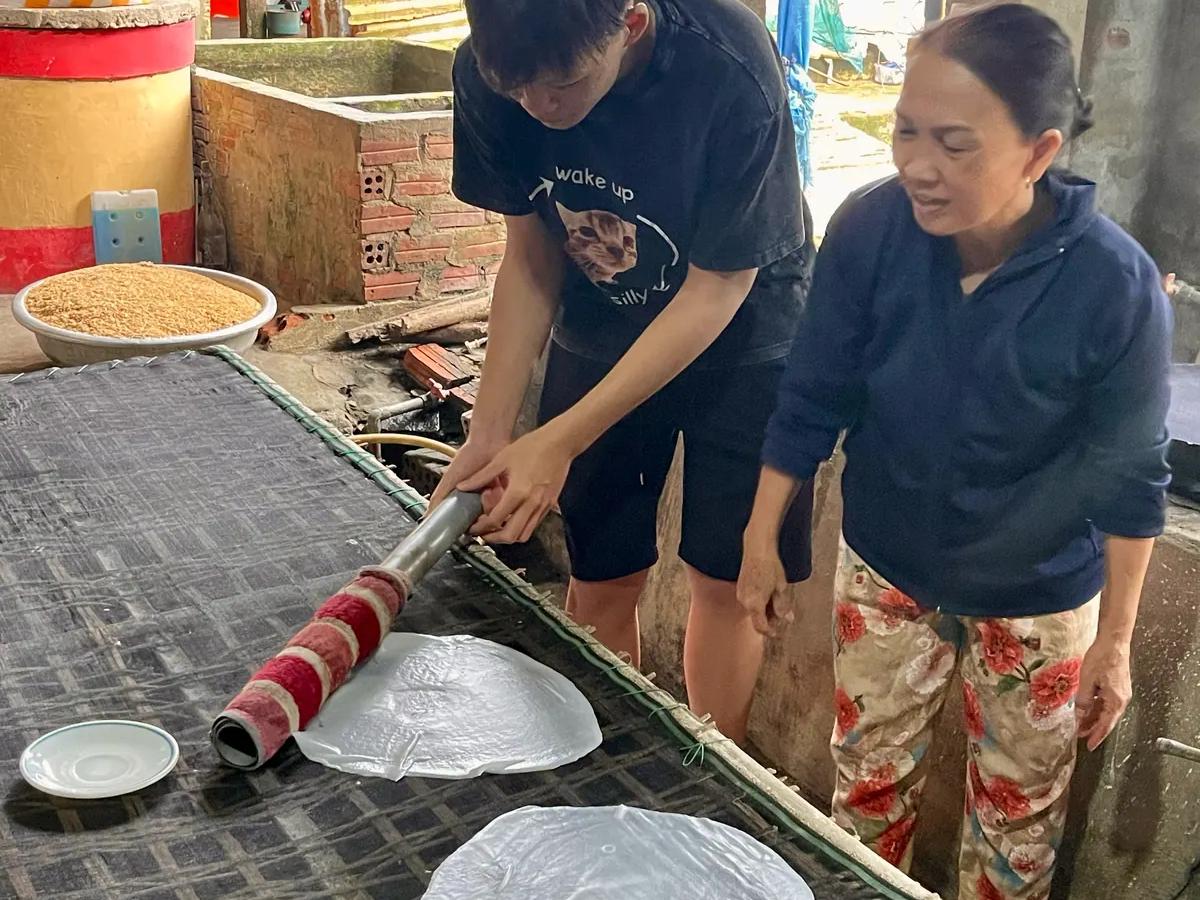 A guest lifting a steamed rice sheet off the cloth with the family who makes the noodles