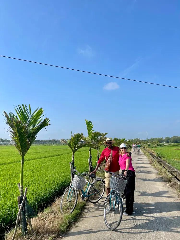 A cyclist on a narrow concrete path between green rice paddies near Hoi An