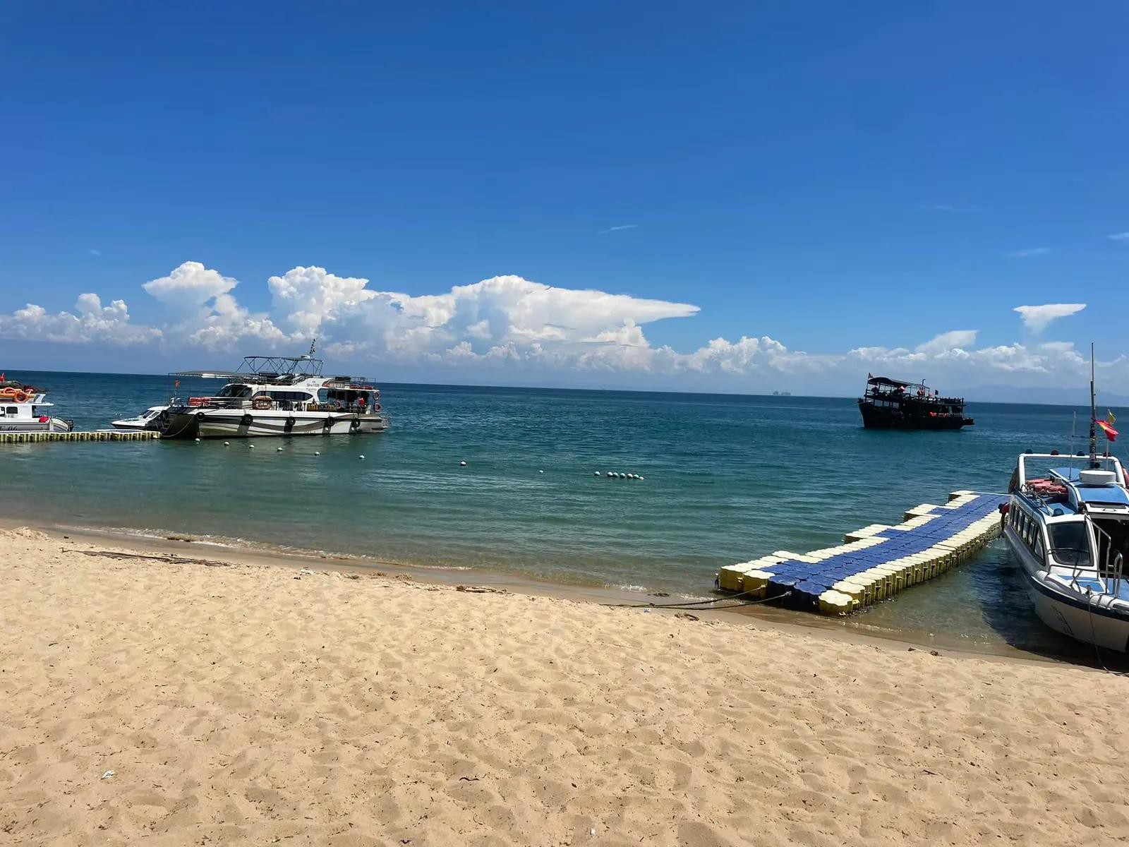 Speedboats moored off a sandy beach on Cham Island, beside a floating jetty in turquoise water