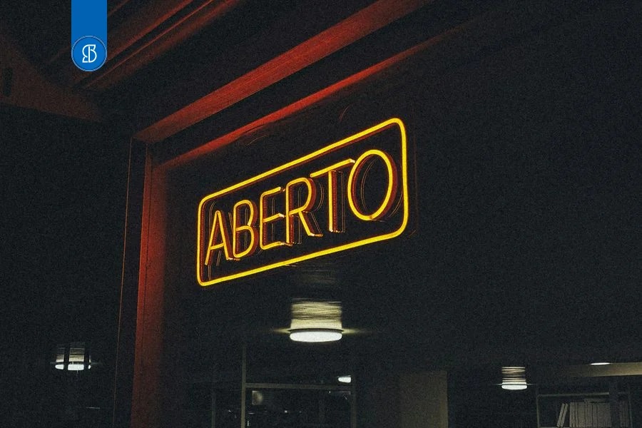 Letreiro de neon amarelo com a palavra Aberto aceso na fachada escura de um estabelecimento, à noite
