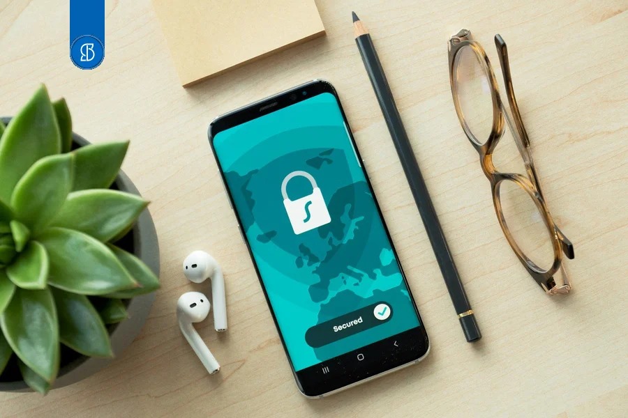 Celular sobre mesa de madeira exibindo um cadeado e a palavra Secured, ao lado de óculos e planta