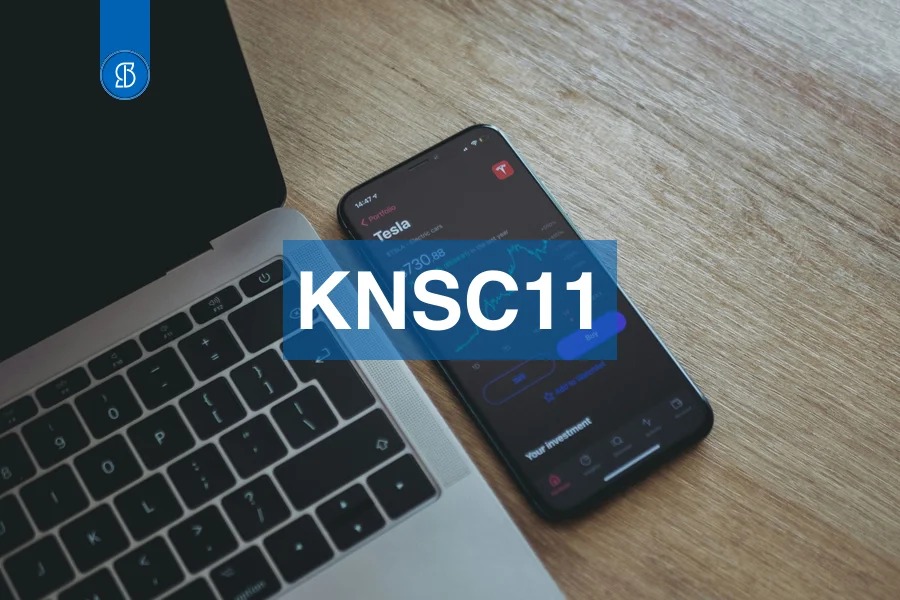 Celular exibindo a cotação de uma ação ao lado de um notebook, com o código KNSC11 em faixa azul ao centro