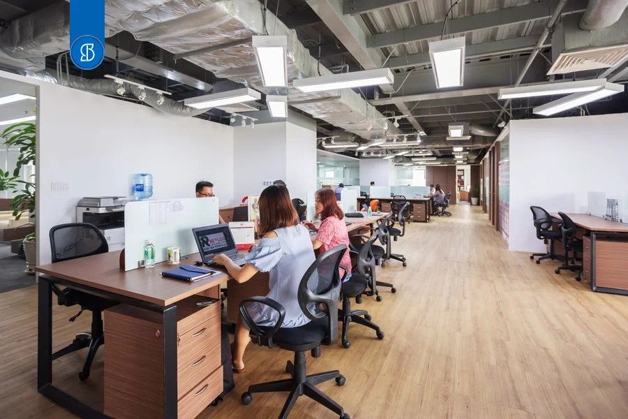 Espaço de coworking com mesas compartilhadas separadas por divisórias baixas e pessoas trabalhando em notebooks