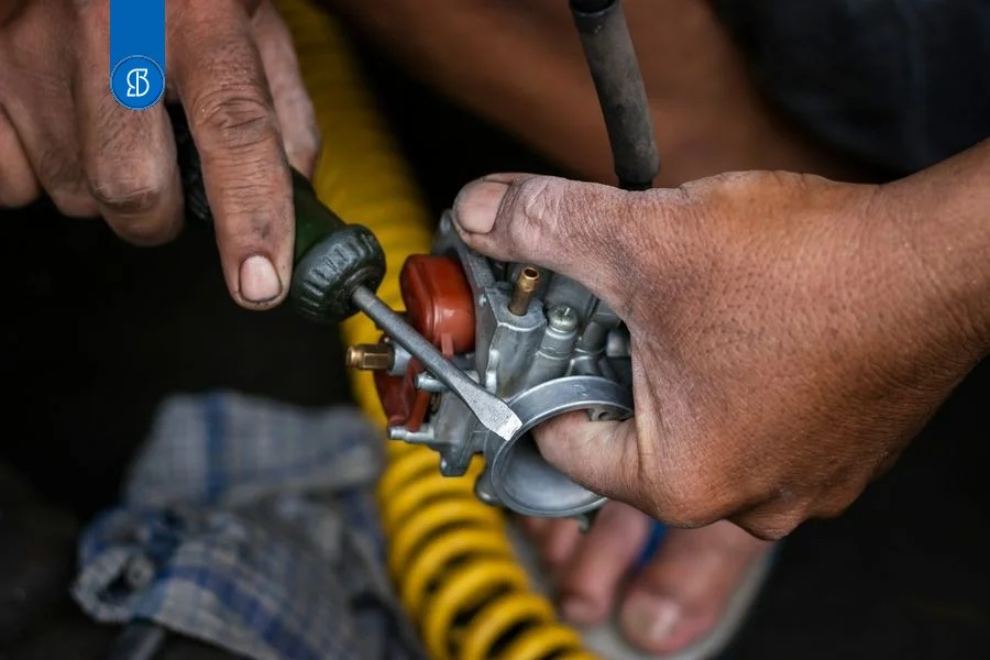 Mãos de um mecânico ajustando um carburador com chave de fenda, em close