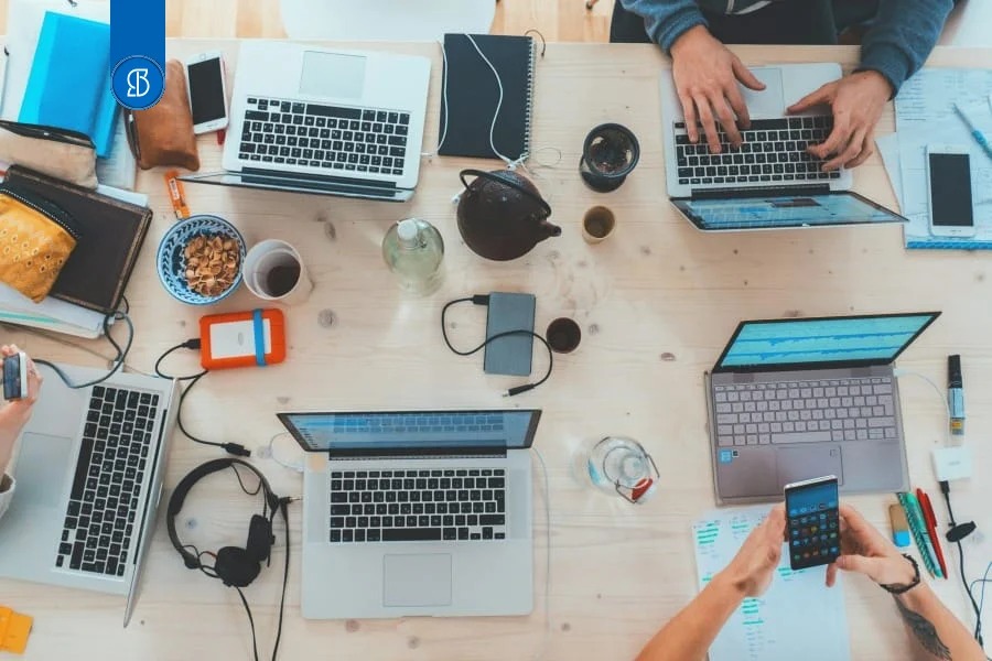 Vista de cima de uma mesa com vários notebooks, cadernos e mãos trabalhando em conjunto