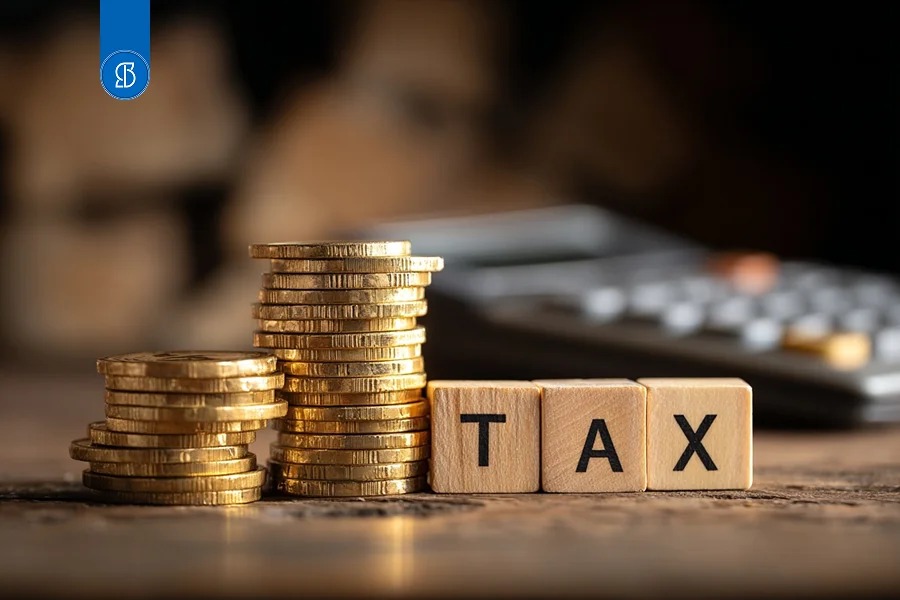 Cubos de madeira formando a palavra TAX ao lado de pilhas de moedas douradas
