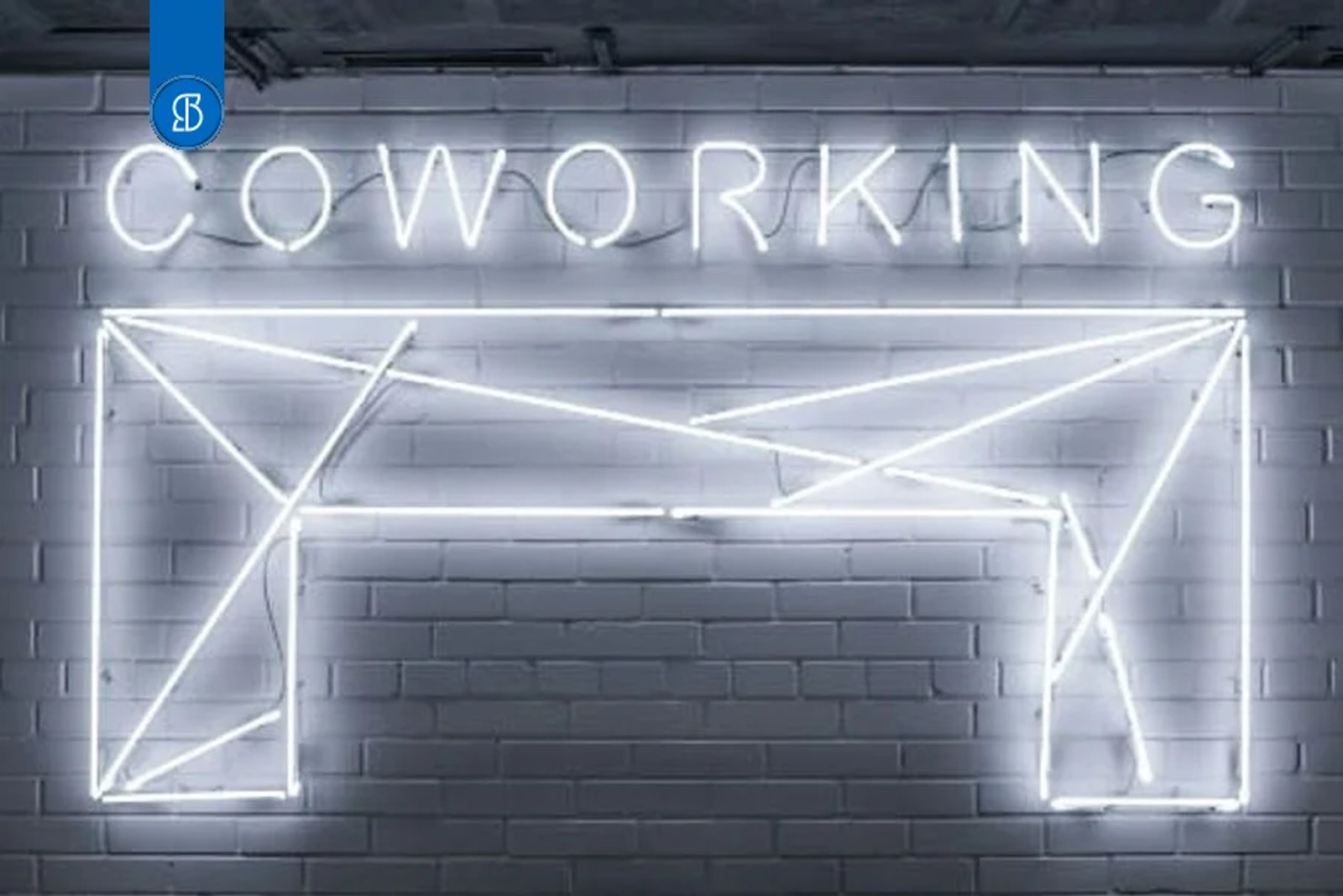 Letreiro de neon branco com a palavra Coworking e o desenho de uma mesa, sobre parede de tijolos pintada