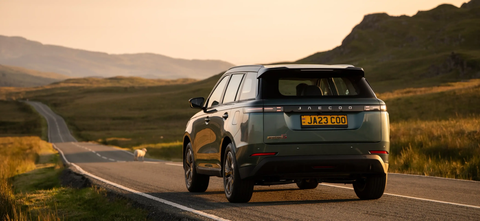 A green JAECOO SUV heading down an open moorland road at dusk
