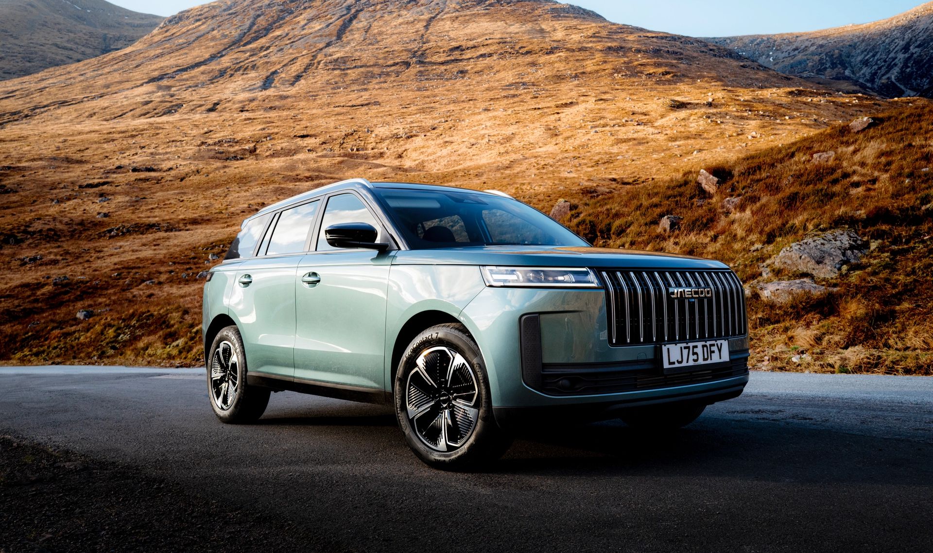A green JAECOO 7 SUV parked in a desert landscape with mountains behind
