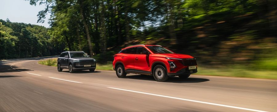 A red OMODA 5 and a JAECOO 5 driving on a tree-lined road
