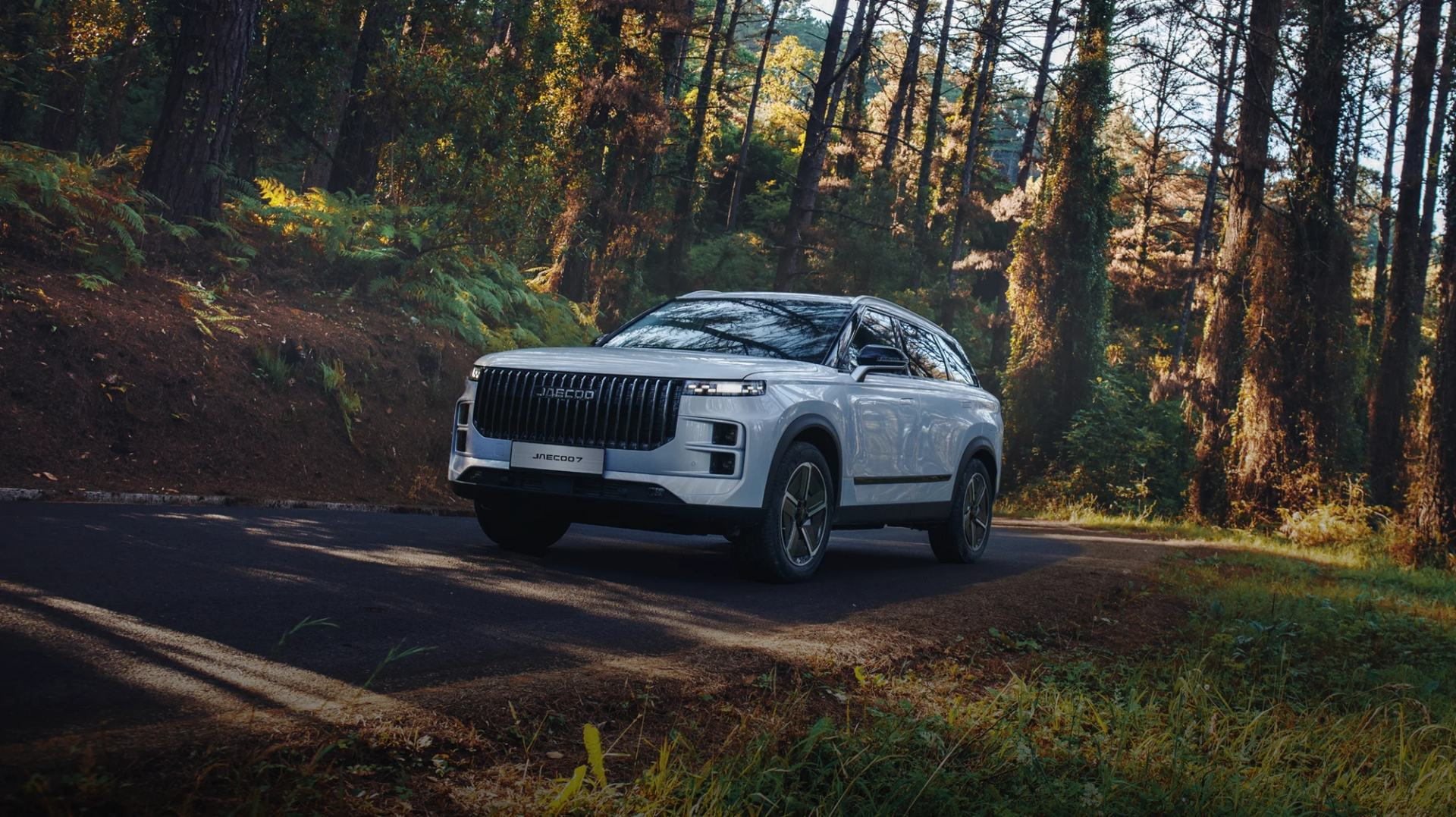 A white JAECOO 7 SUV driving along a tree-lined country road