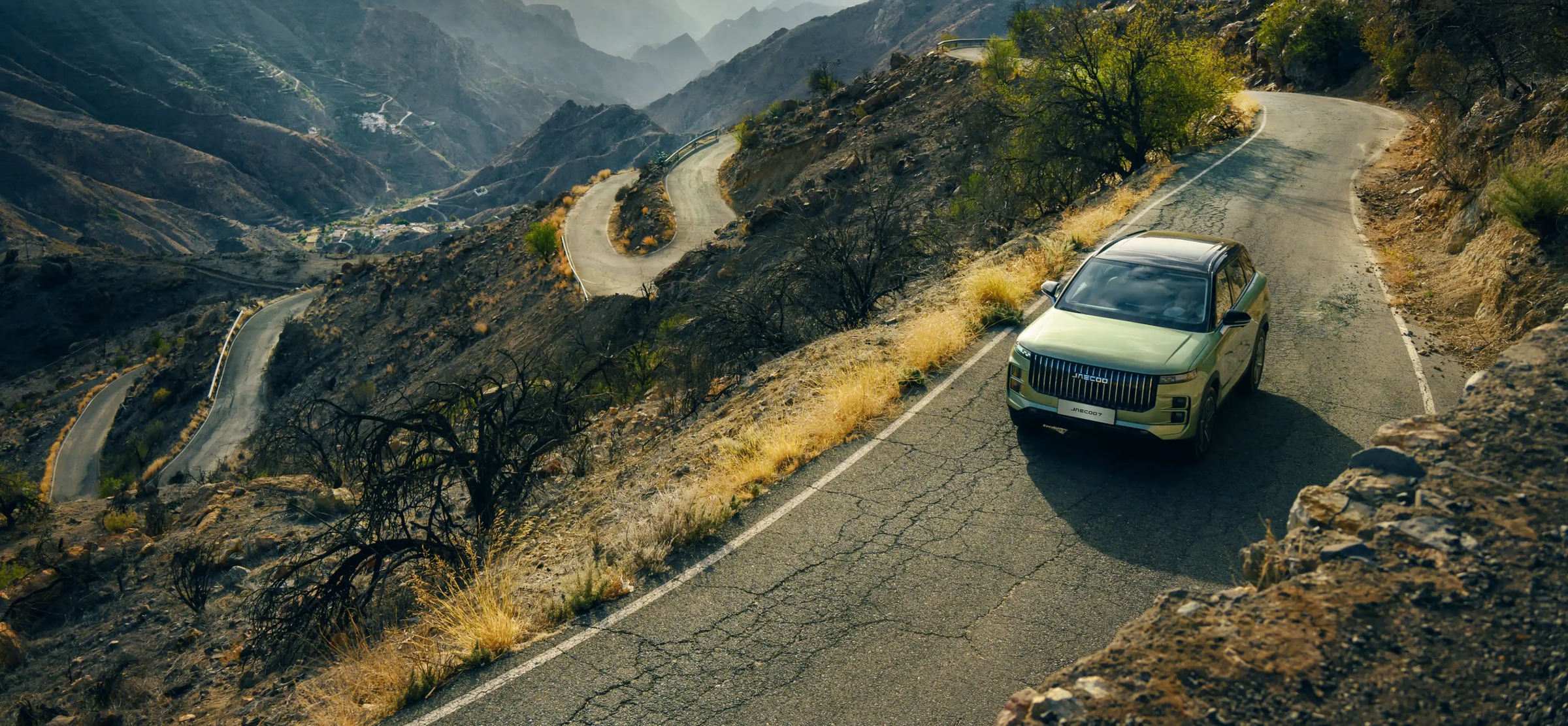 A green JAECOO SUV on a winding mountain road at golden hour