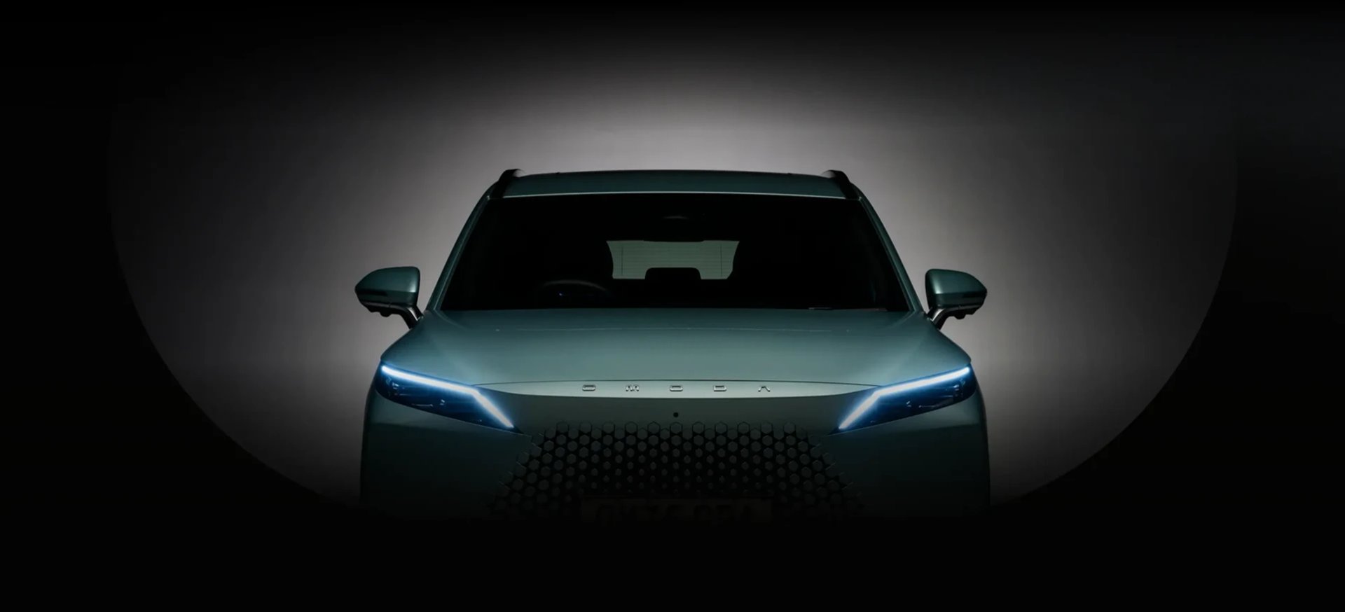Close-up front view of an OMODA 7 headlight and grille in dramatic lighting