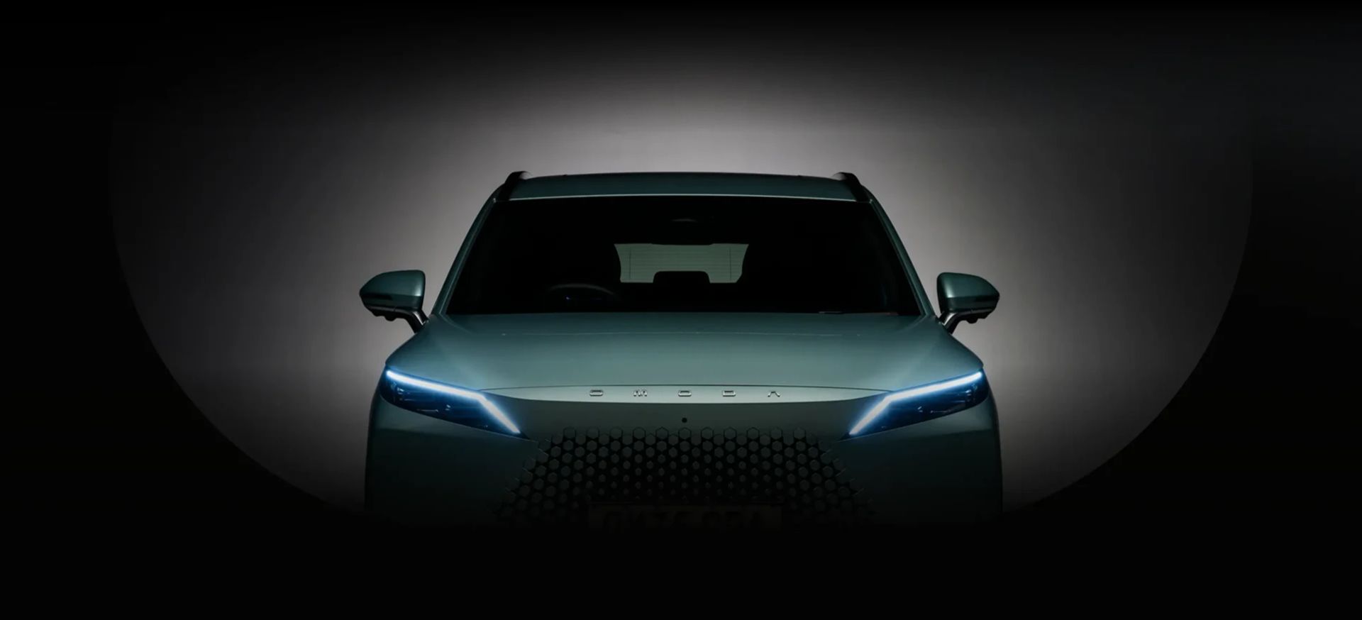 Close-up front view of an OMODA 7 headlight and grille in dramatic lighting