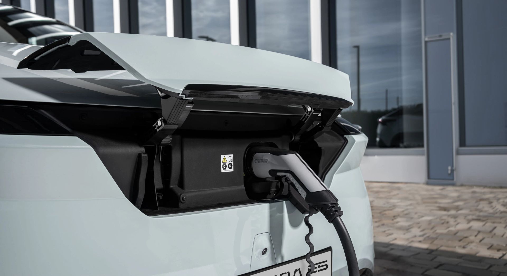 Charging cable plugged into the rear port of a pale green electric OMODA outside a dealership
