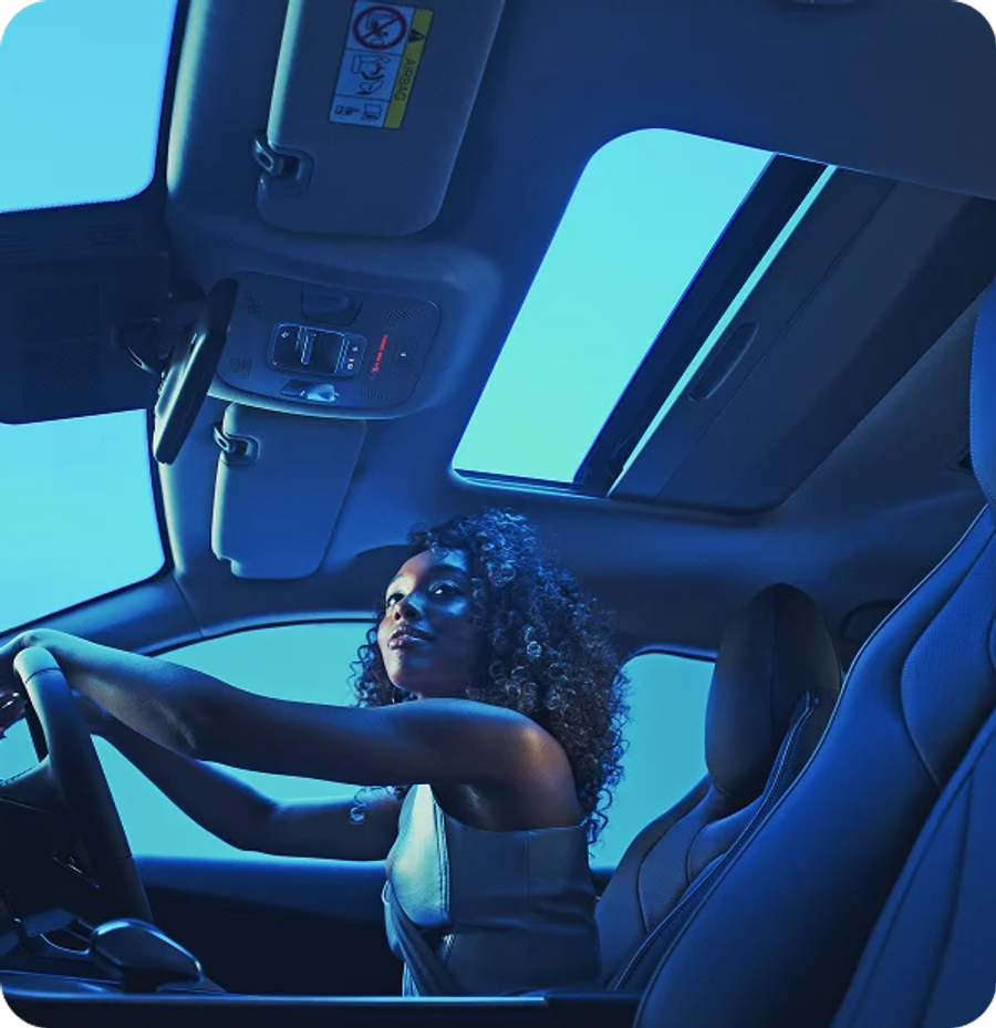 Woman driving at night with the panoramic sunroof visible in blue ambient light