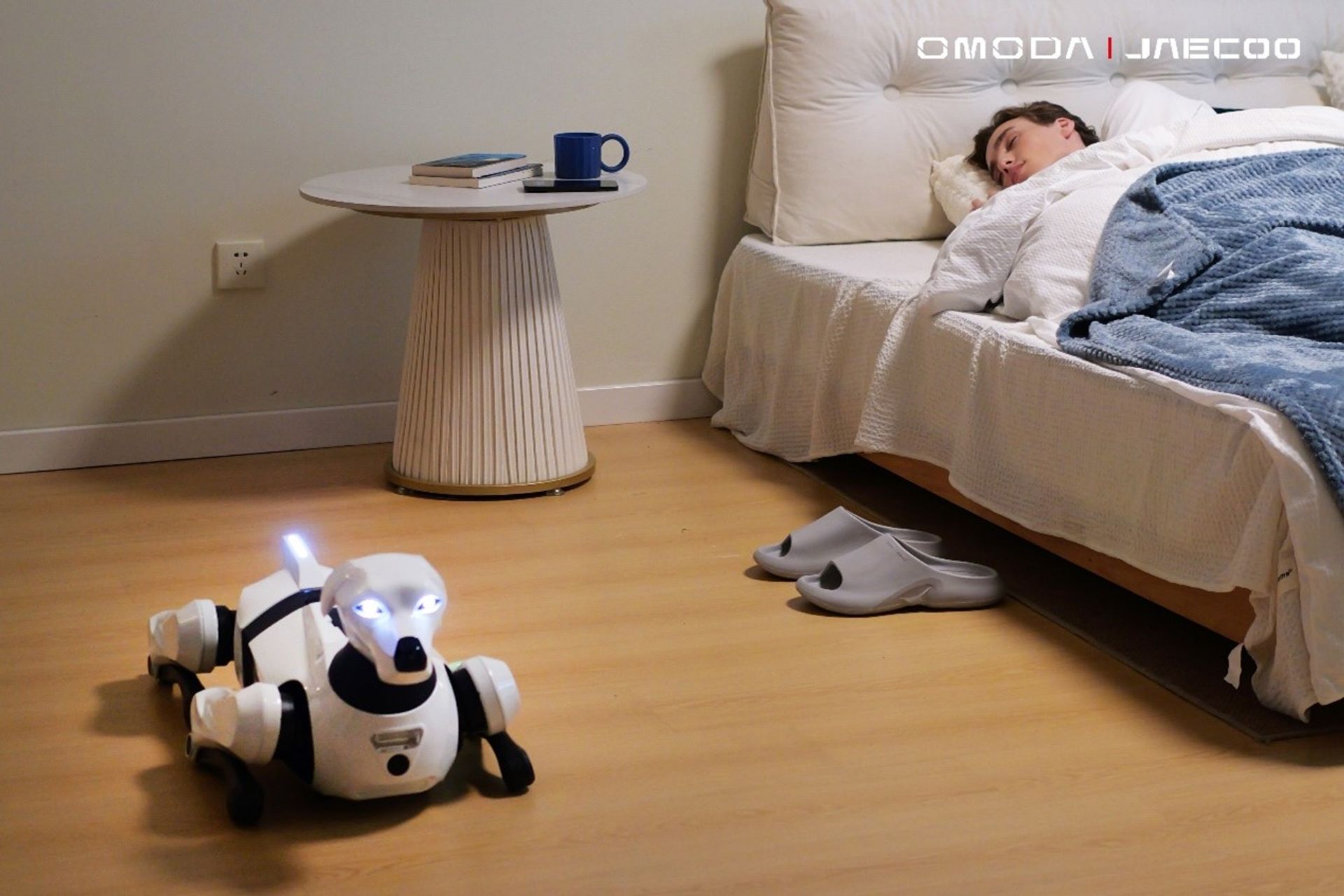 Small robotic companion dog toy on the floor beside a sleeping person's bed