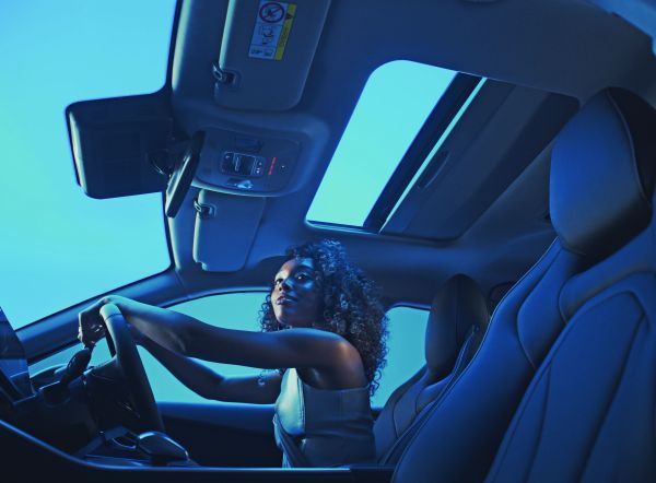 Woman driving with an open panoramic sunroof lit in blue tones