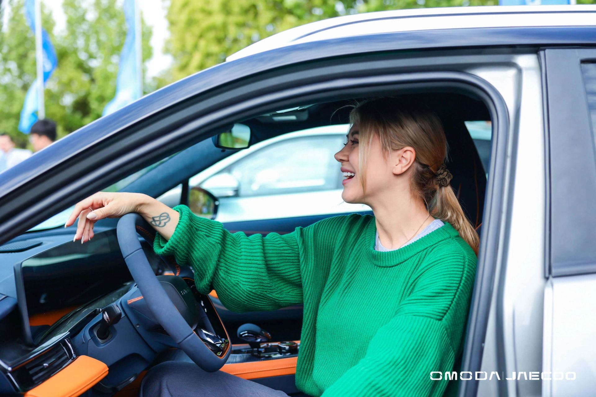 Woman smiling behind the wheel of a silver SUV with orange trim