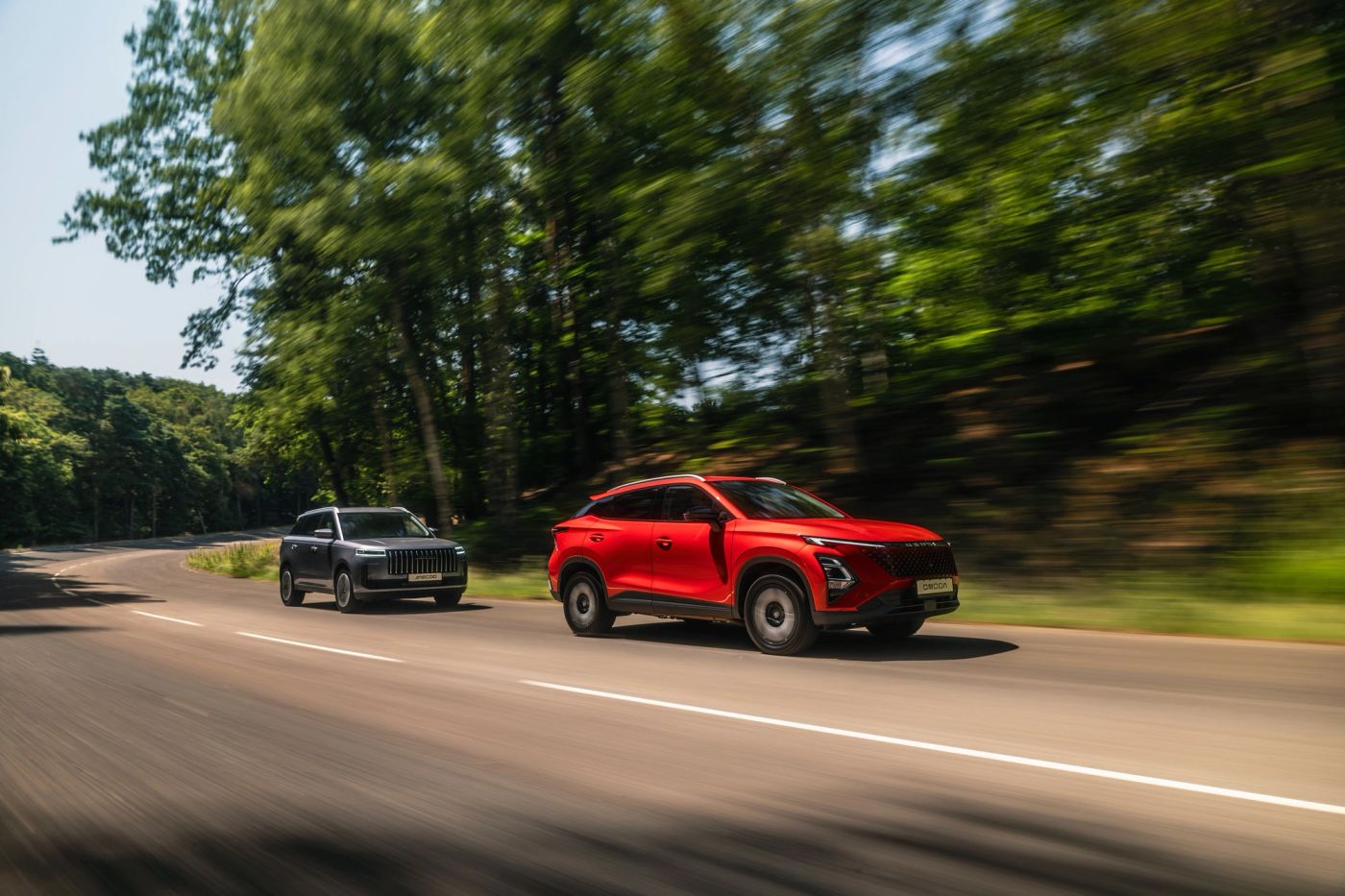 A red OMODA 5 and a JAECOO 5 driving on a tree-lined road