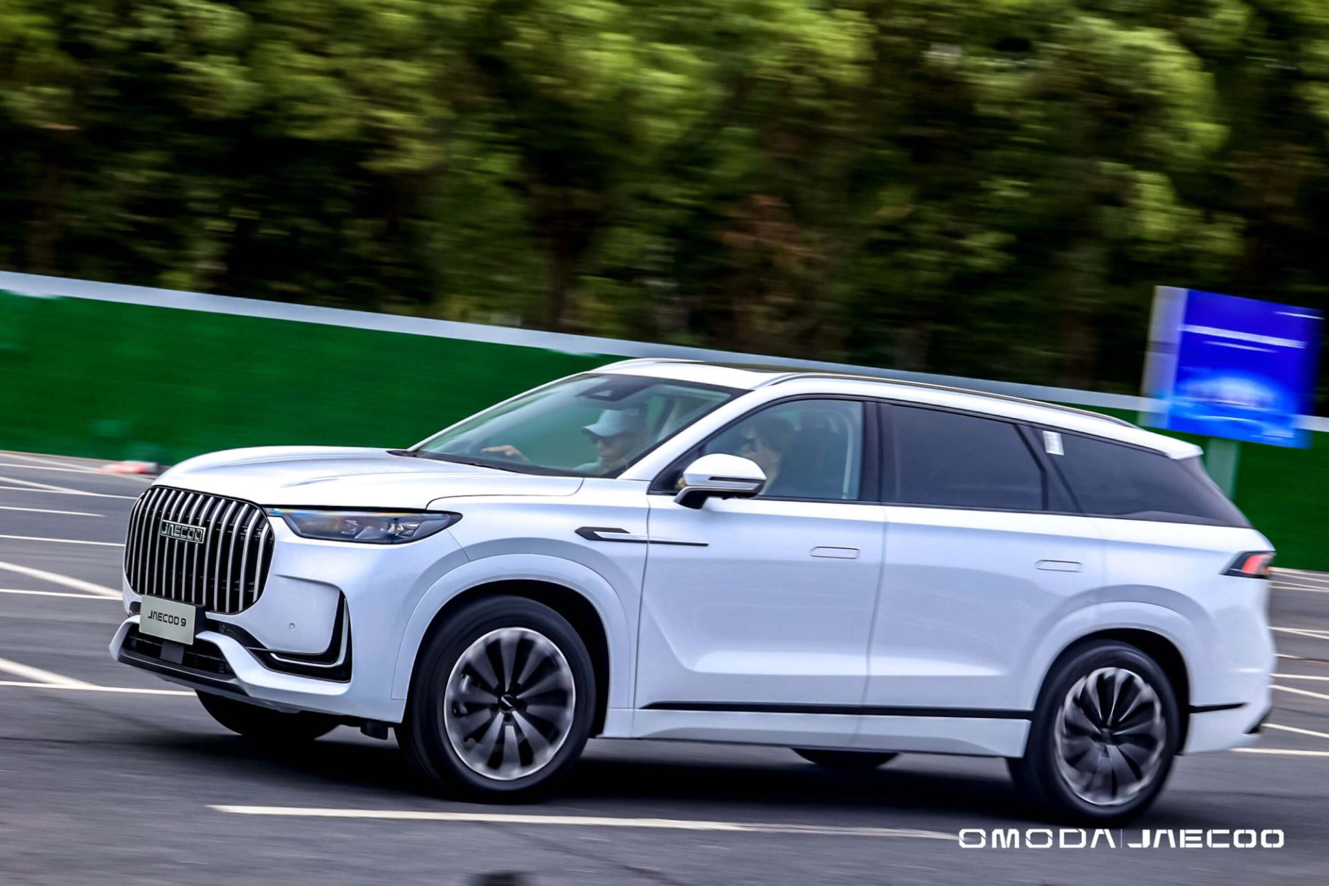 White SUV driving at speed along a tree-lined test track