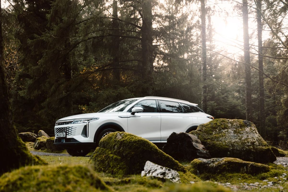 A white OMODA SUV parked in a forest clearing