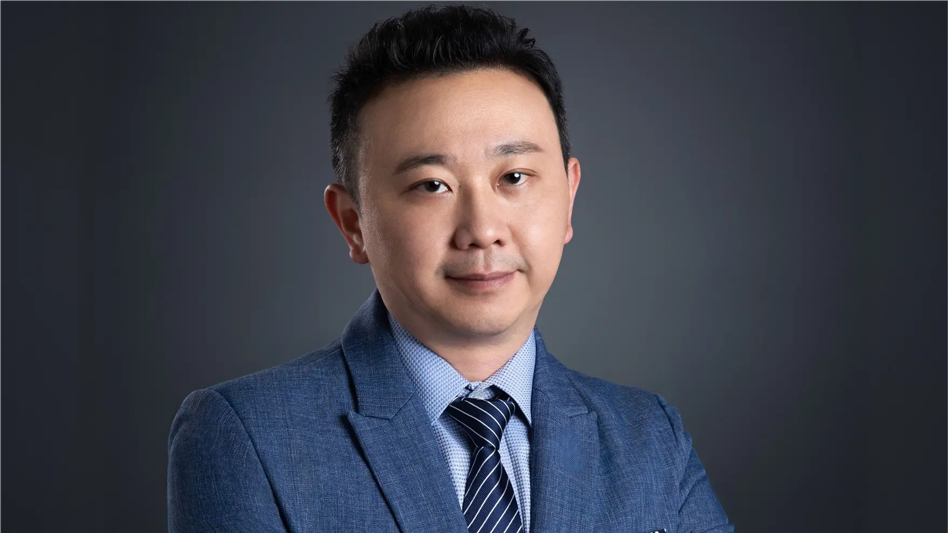 Corporate headshot of a smartly dressed man against a plain grey background