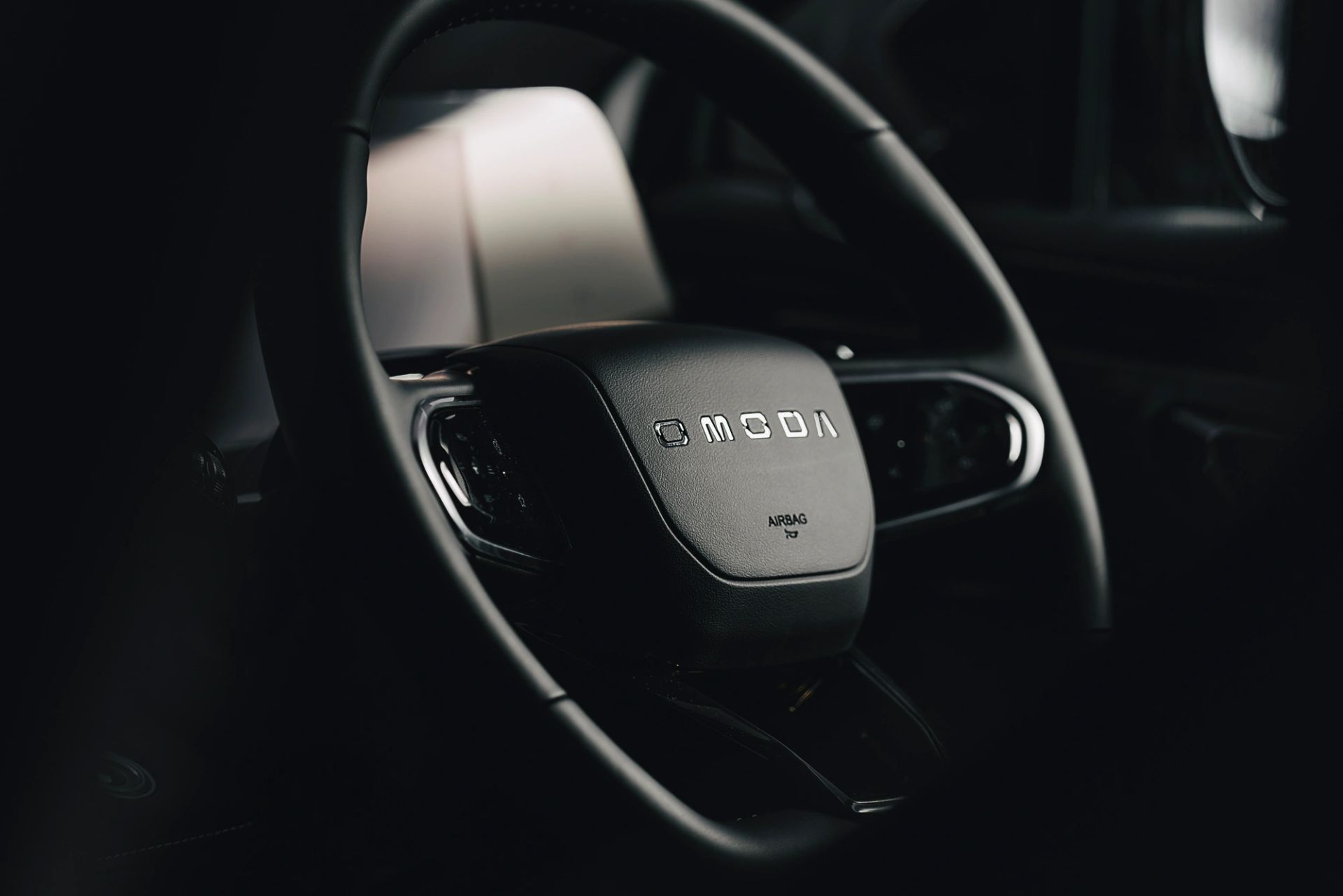 Close-up of an OMODA steering wheel badge in a dark interior