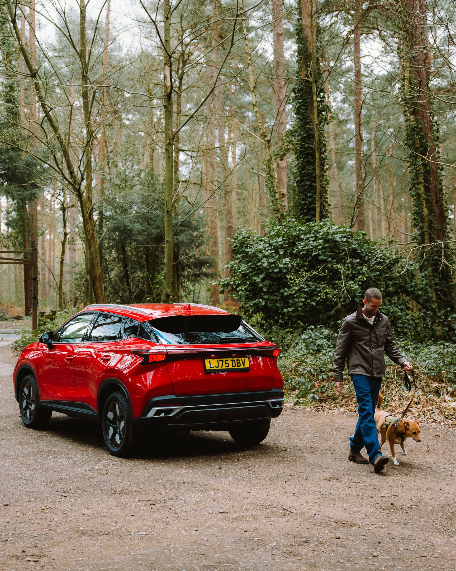 Red OMODA SUV parked on a forest track with a person walking a dog