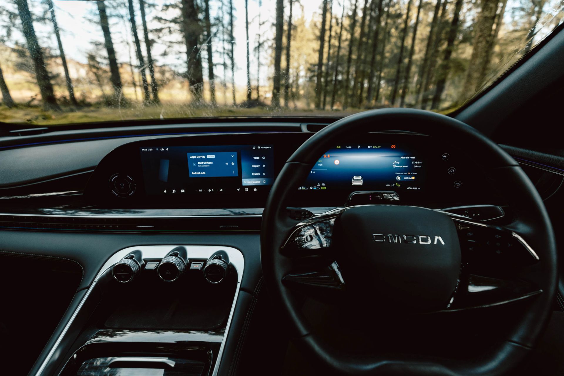OMODA driver's interior view showing dual screens and forest scenery ahead