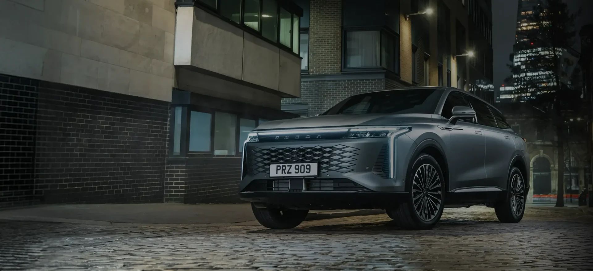 An OMODA SUV parked on a cobbled street in a city at night