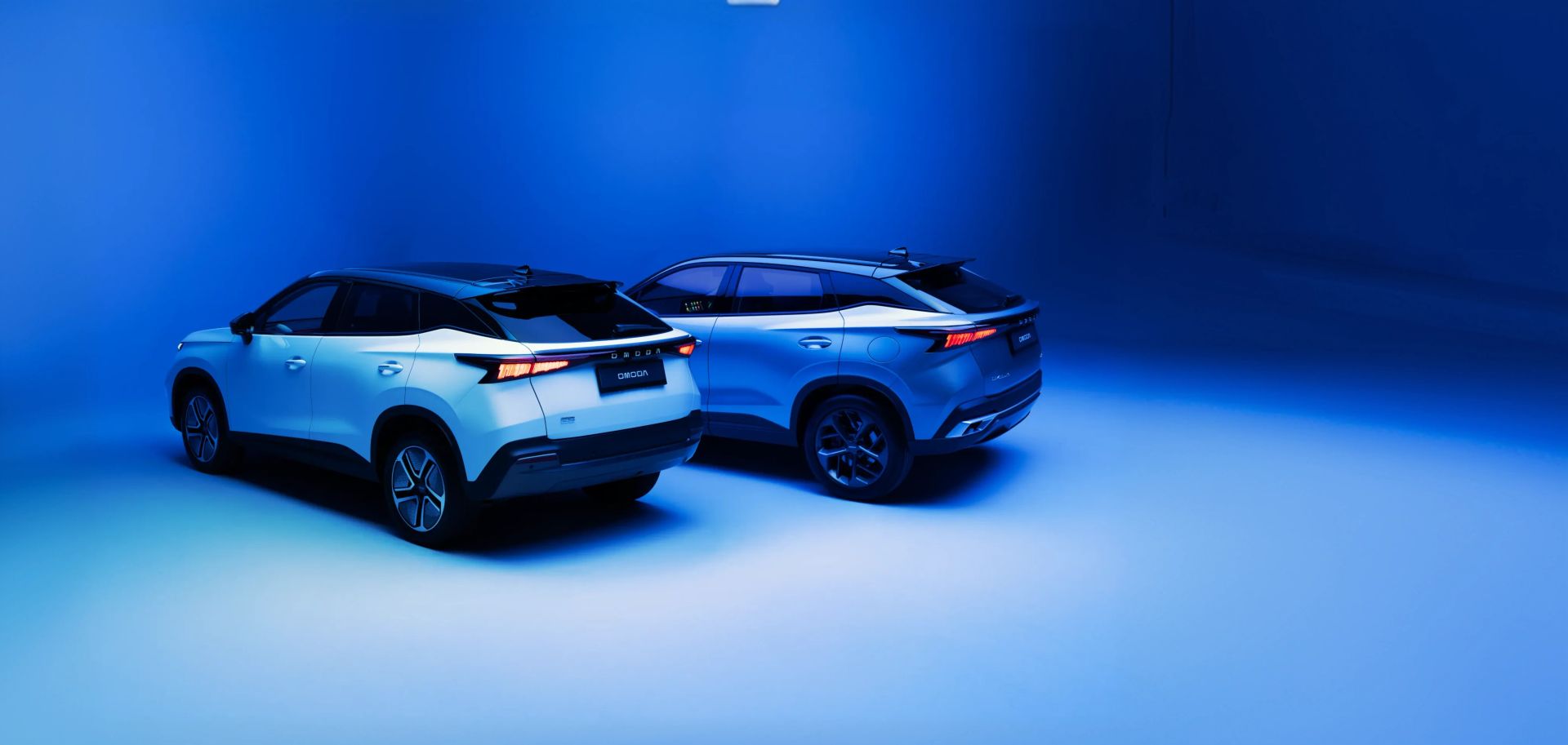 Two OMODA SUVs lit on a blue studio backdrop