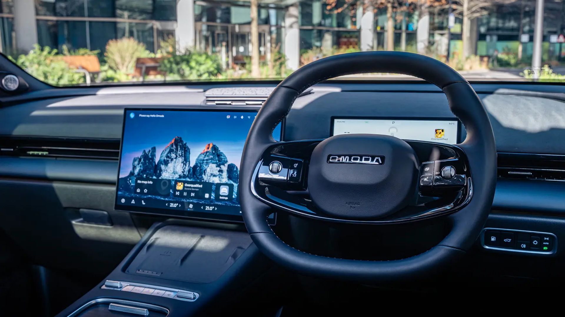 OMODA interior showing steering wheel and dashboard screens with a glass building outside the windscreen