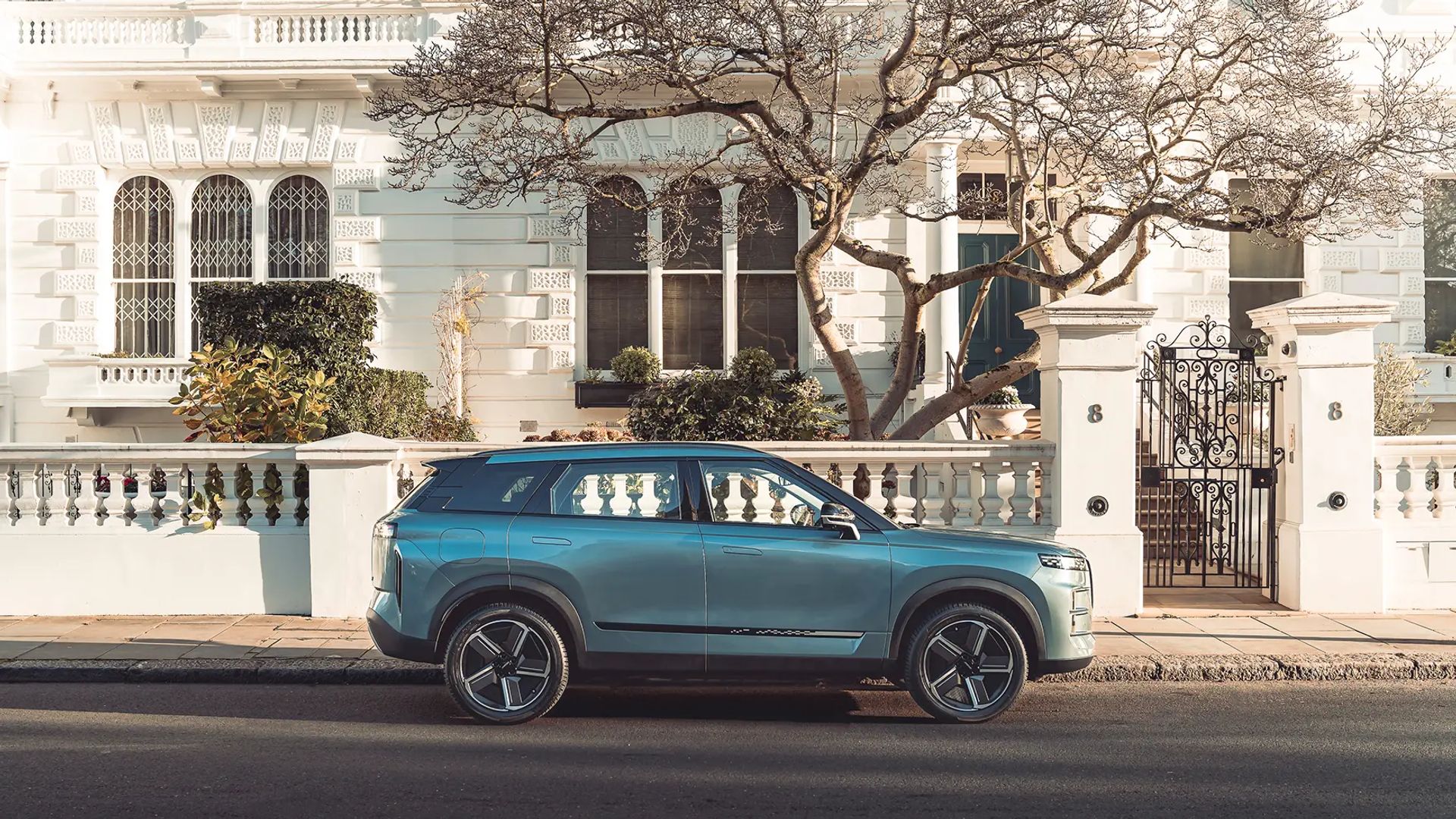 Teal-blue SUV parked kerbside outside period white townhouses on a residential street