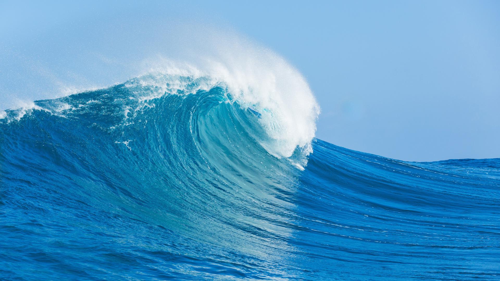 arge ocean wave curling under a clear blue sky, ideal for surfing.